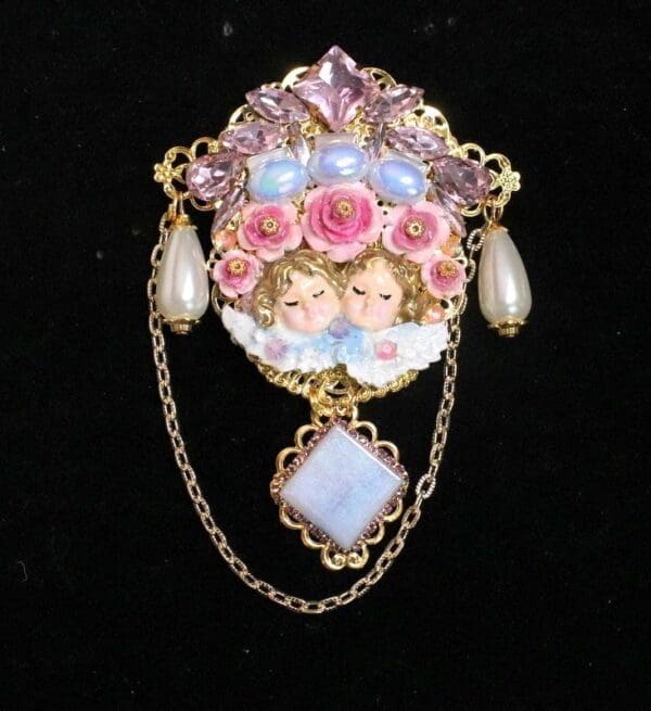 A brooch with two angels and roses on it.