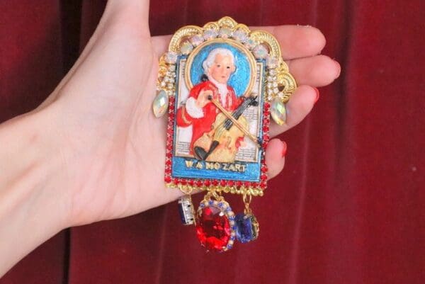 A hand holding a small painting of a man playing the violin.