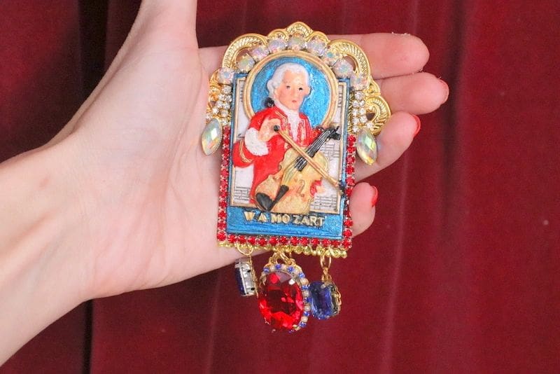 A hand holding a small painting of a man playing the violin.