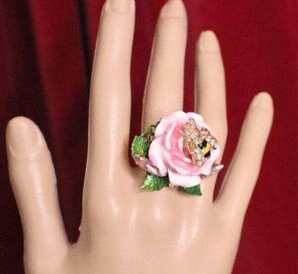 A hand wearing a ring with a pink flower on it