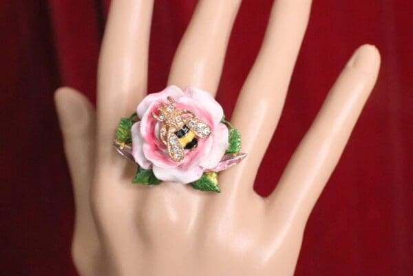 A hand wearing a ring with a flower on it