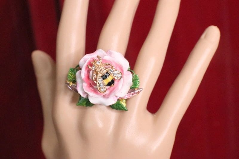 A hand wearing a ring with a flower on it