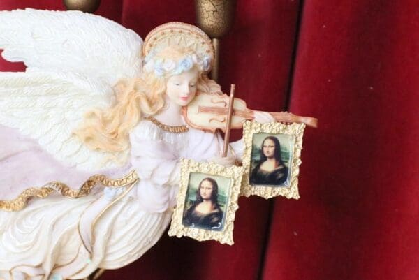 A doll holding two pictures of the mona lisa.