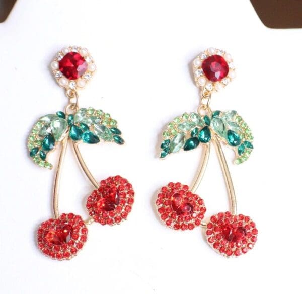 A pair of earrings with red cherries and green leaves.