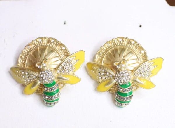 A pair of gold earrings with green and yellow bee.
