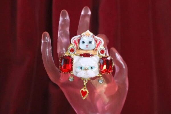A hand holding a cat pin with red stones.