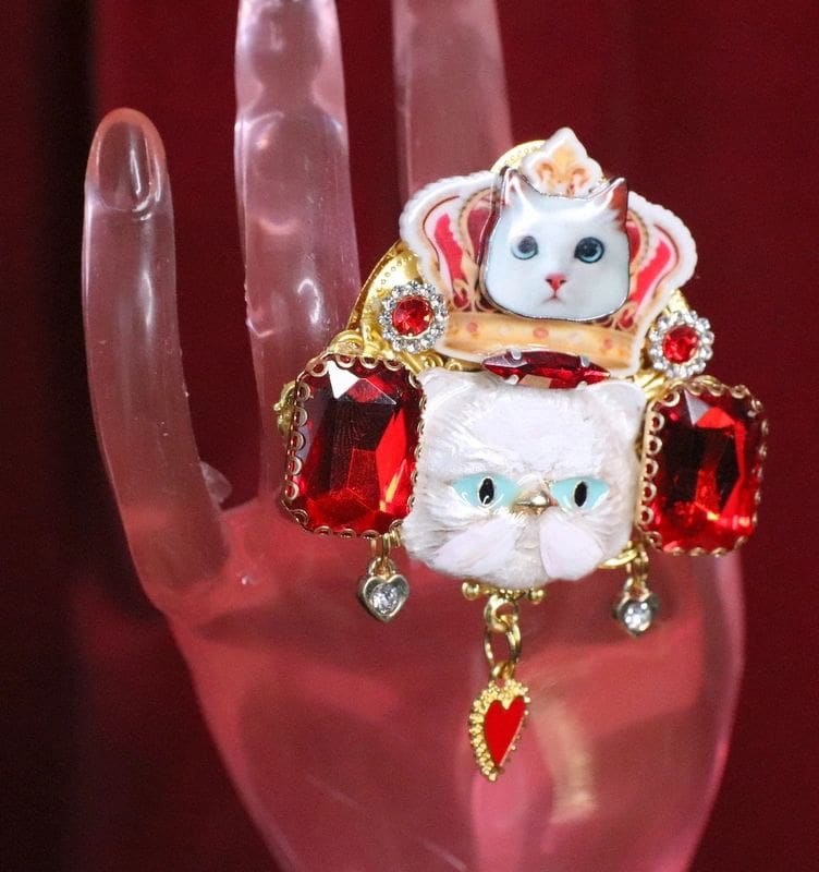 A hand holding a cat brooch with red and gold accents.