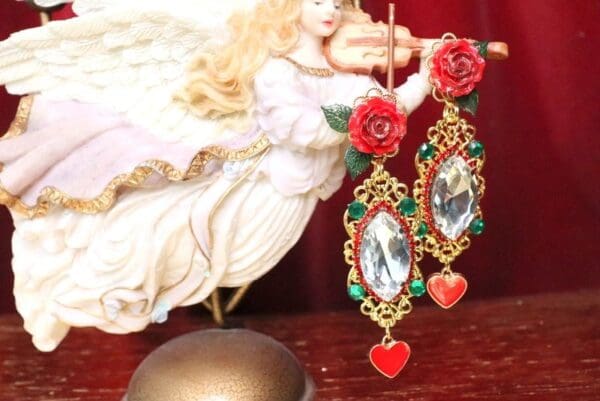 A pair of earrings with red roses and green leaves.