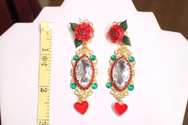 A pair of earrings with red roses and hearts.
