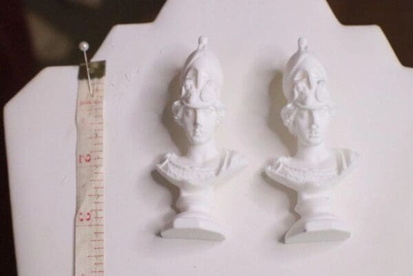 Two white statues are on a table next to a ruler.