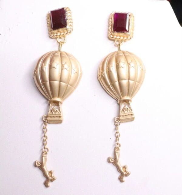 A pair of gold earrings with red stones hanging from the bottom.