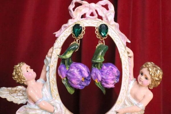 A pair of earrings with purple flowers and green leaves.