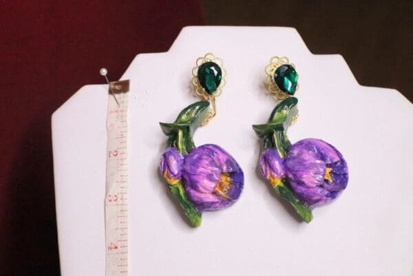 A pair of earrings with purple flowers and green stones.