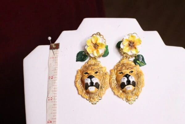 A pair of earrings with yellow flowers and a lion head.