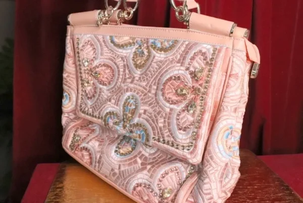 A pink purse with a large ornate pattern on it.