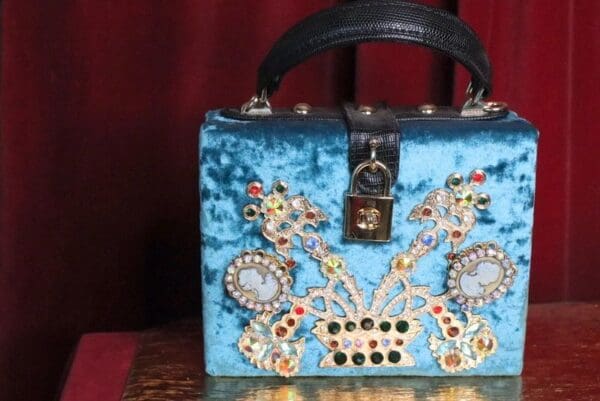 A blue purse with many different colored jewels.