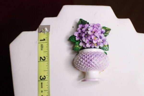 A small white vase with purple flowers in it.