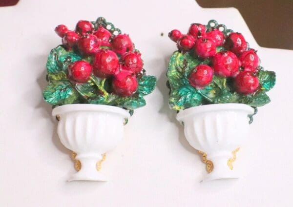 A pair of white wall hanging with red berries in it.