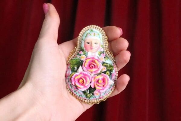 A hand holding a small doll with pink roses.
