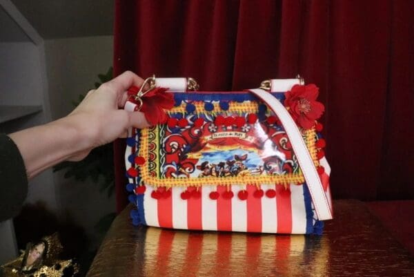 A hand is holding onto a circus themed purse.
