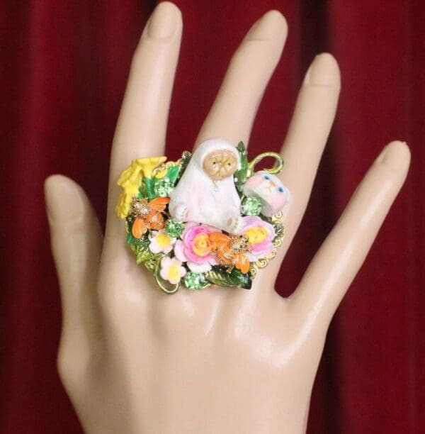A hand wearing a ring with flowers and a bird on it.