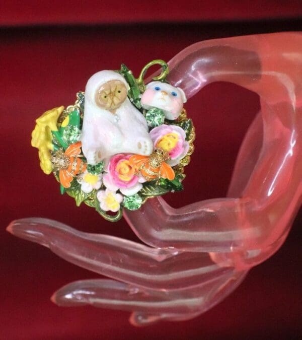 A hand holding a ring with flowers and a bird on it.