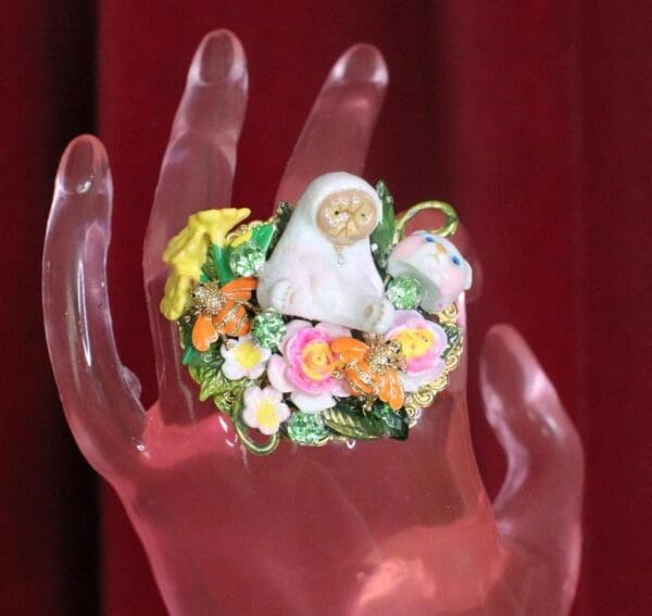 A hand holding a ring with flowers and a statue of jesus.