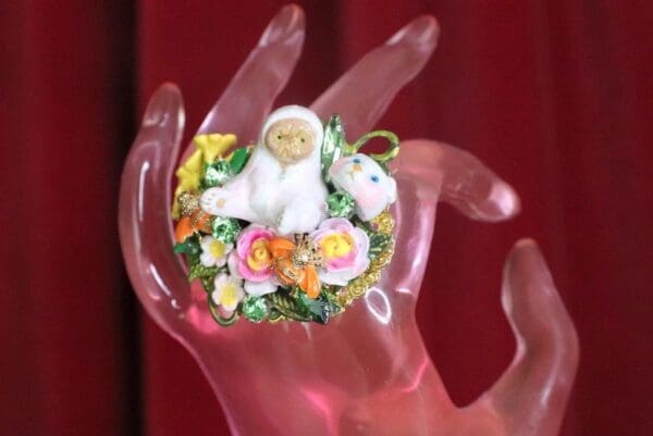 A hand holding a small doll with flowers on it.