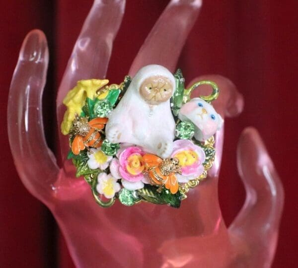 A hand with a ring on it and some flowers around the finger.