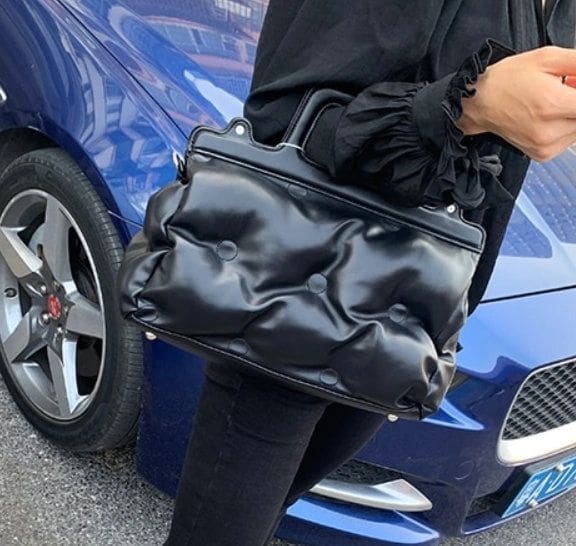 A woman is holding onto her purse while standing next to a car.