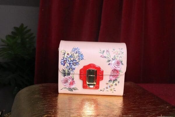A pink purse with flowers on it sitting on top of a table.