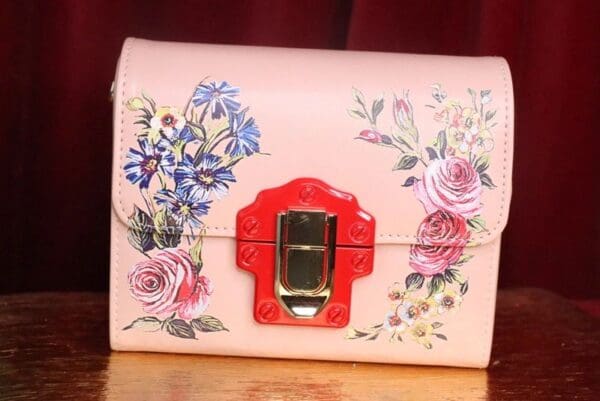 A pink purse with flowers on it sitting on top of a table.