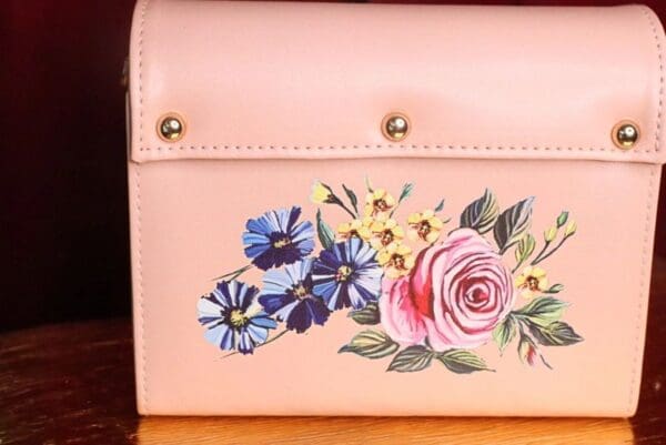 A close up of the front of a pink purse with flowers painted on it.