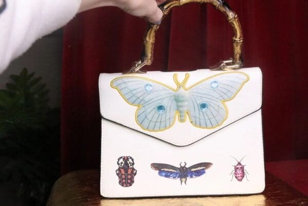 A woman is holding onto a white purse with butterflies on it.