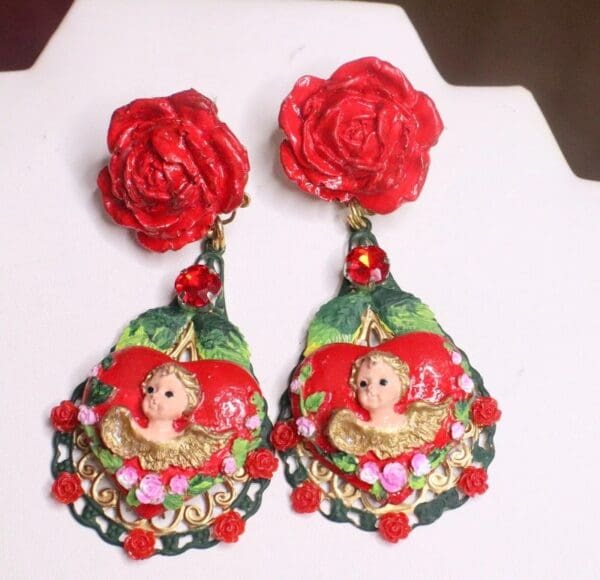 A pair of earrings with red roses and a woman 's face.