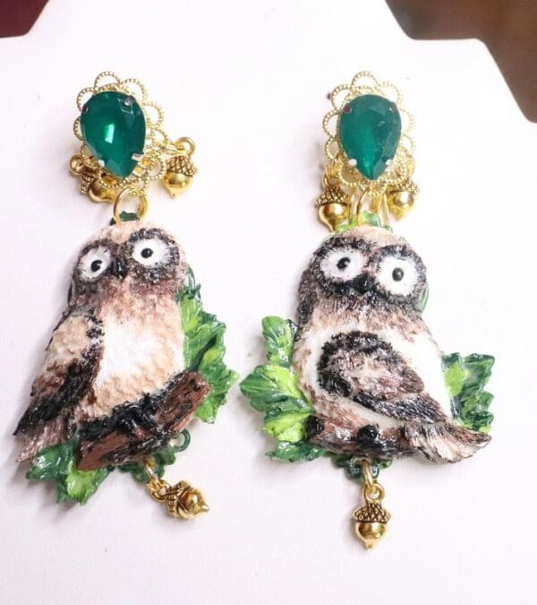 A pair of earrings with an owl and leaves.