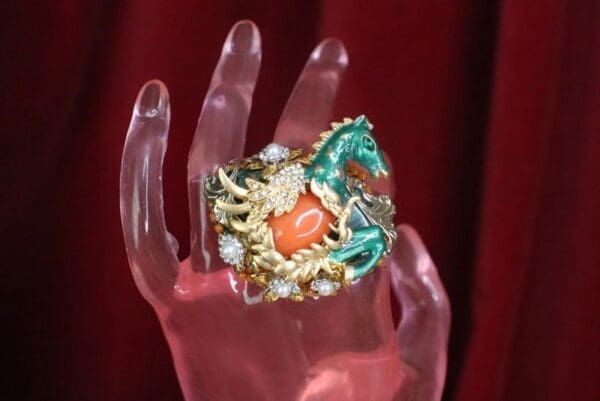 A hand holding a ring with a horse on it.
