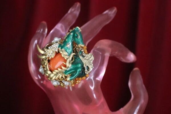 A pink hand holding a red and green ring.