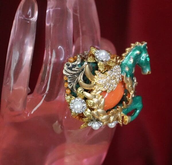 A hand holding a horse brooch with pearls and stones.