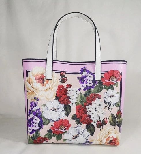 A purple and white floral purse is sitting on the floor.