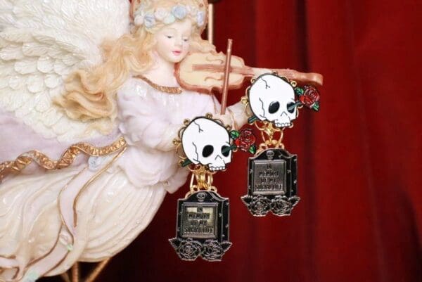 A pair of earrings with skulls and a fairy.