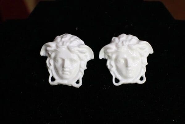 A pair of white versace earrings on black velvet.
