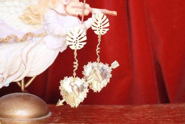 A pair of gold earrings hanging from a red curtain.