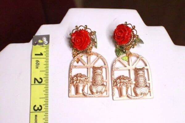 A pair of earrings with red roses and gold elephants.