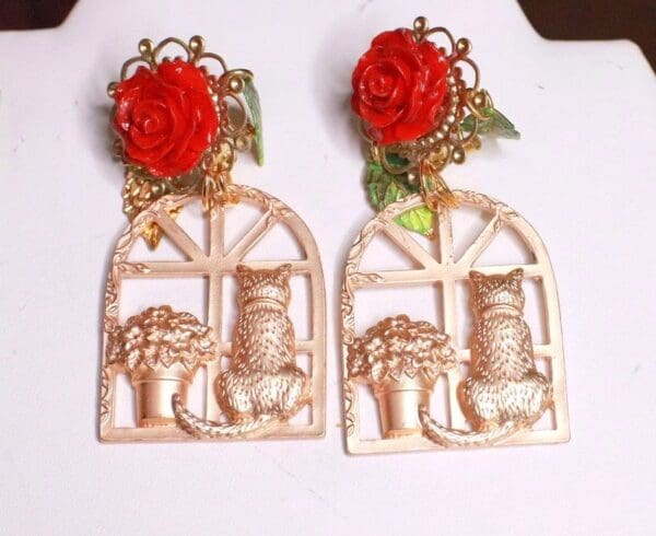 A pair of earrings with roses and cat in the window.