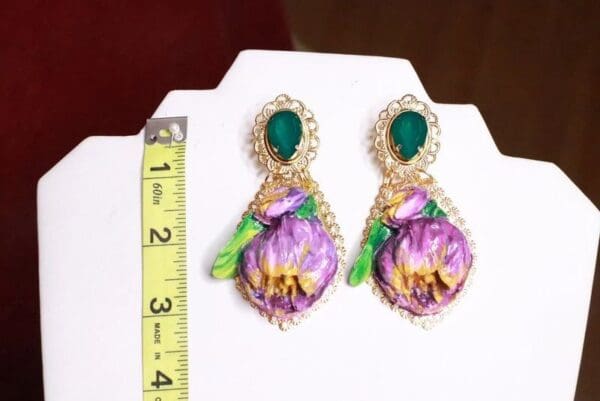 A pair of earrings with purple flowers and green leaves.