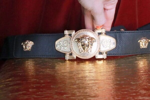 A person is holding onto the belt of a versace belt.
