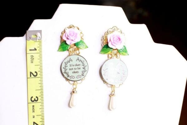 A pair of earrings with pink flowers and a gold frame.
