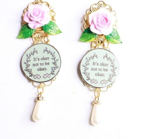 A pair of earrings with pink roses and a quote.