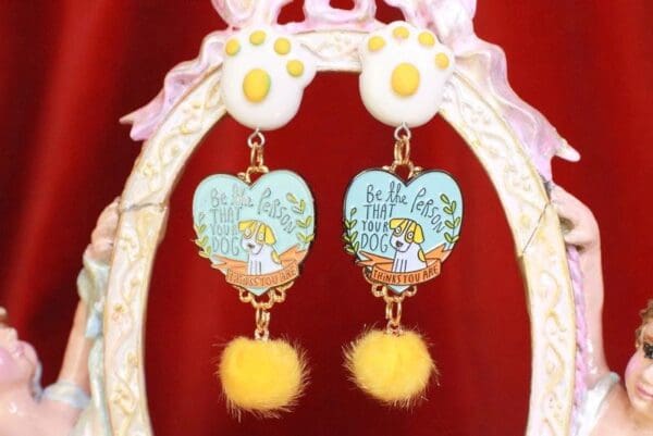 A pair of earrings with yellow fur and a heart shaped picture.